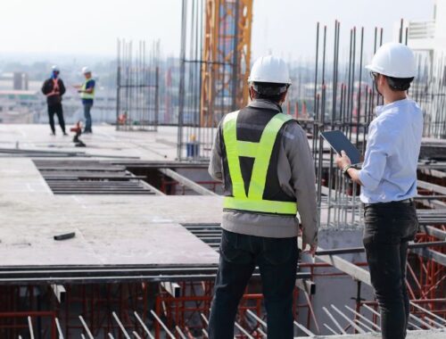 lavoratori in un cantiere edile sotto il sole, con operai che si rinfrescano o indossano indumenti protettivi